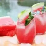 two glasses of watermelon vodka cocktail with slices of watermelon beside a swimming pool.