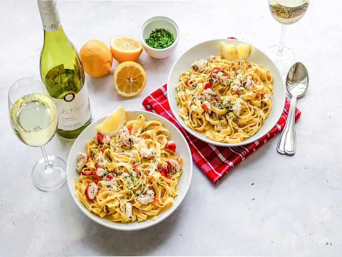 Two bowls of lobster fettuccine with a bottle of viognier wine.