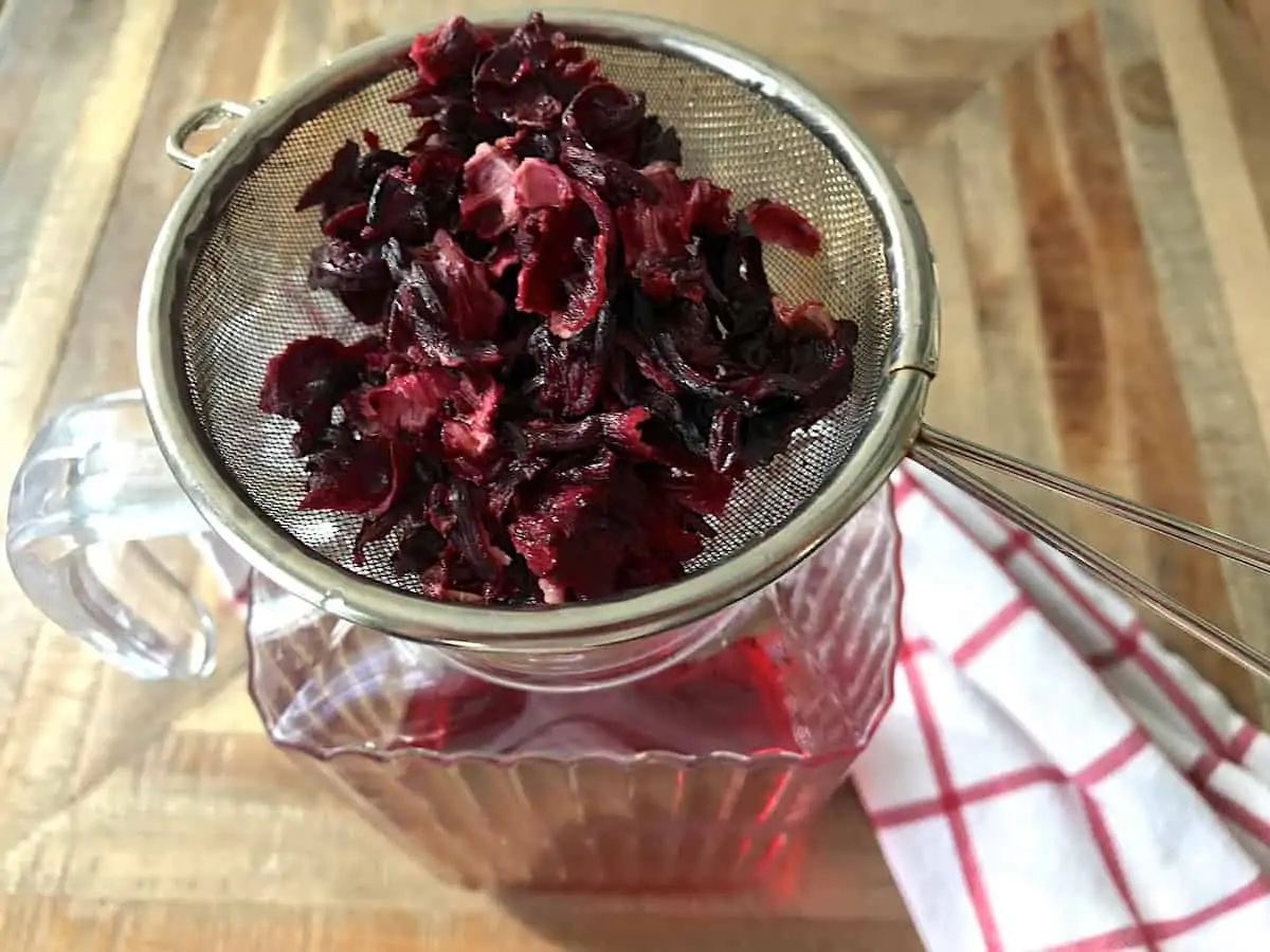 Hibiscus flowers being strained into a glass jar.