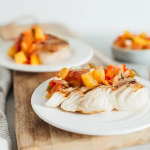 two pieces of grilled halibut with peach salsa on white plates.