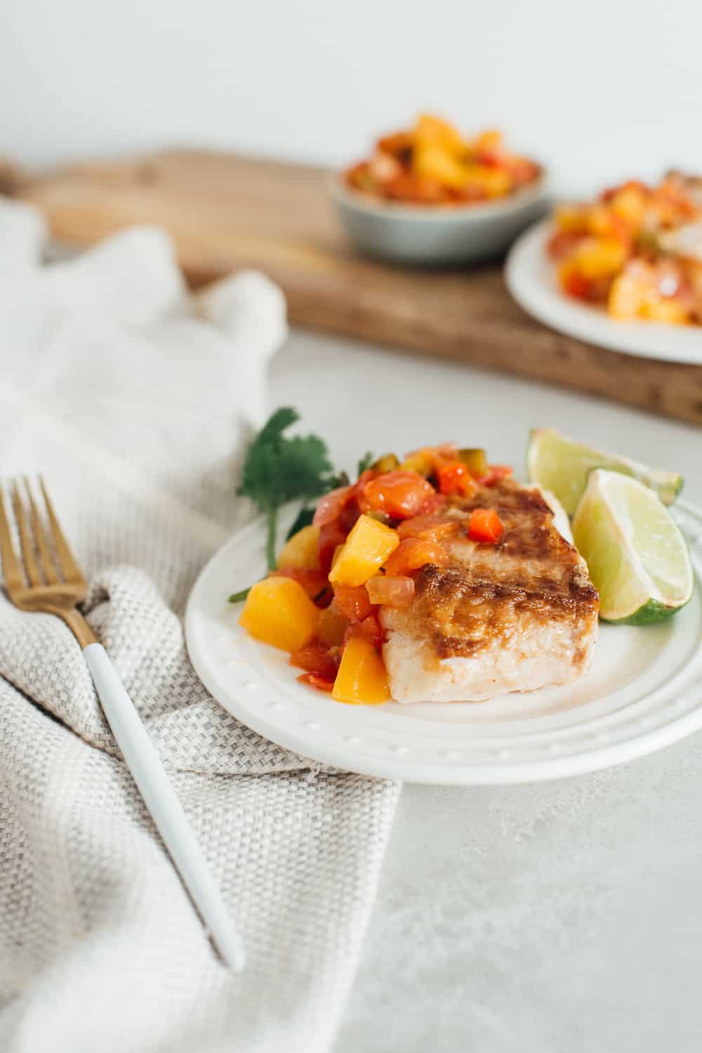 Grilled halibut with peach salsa on a white plate.