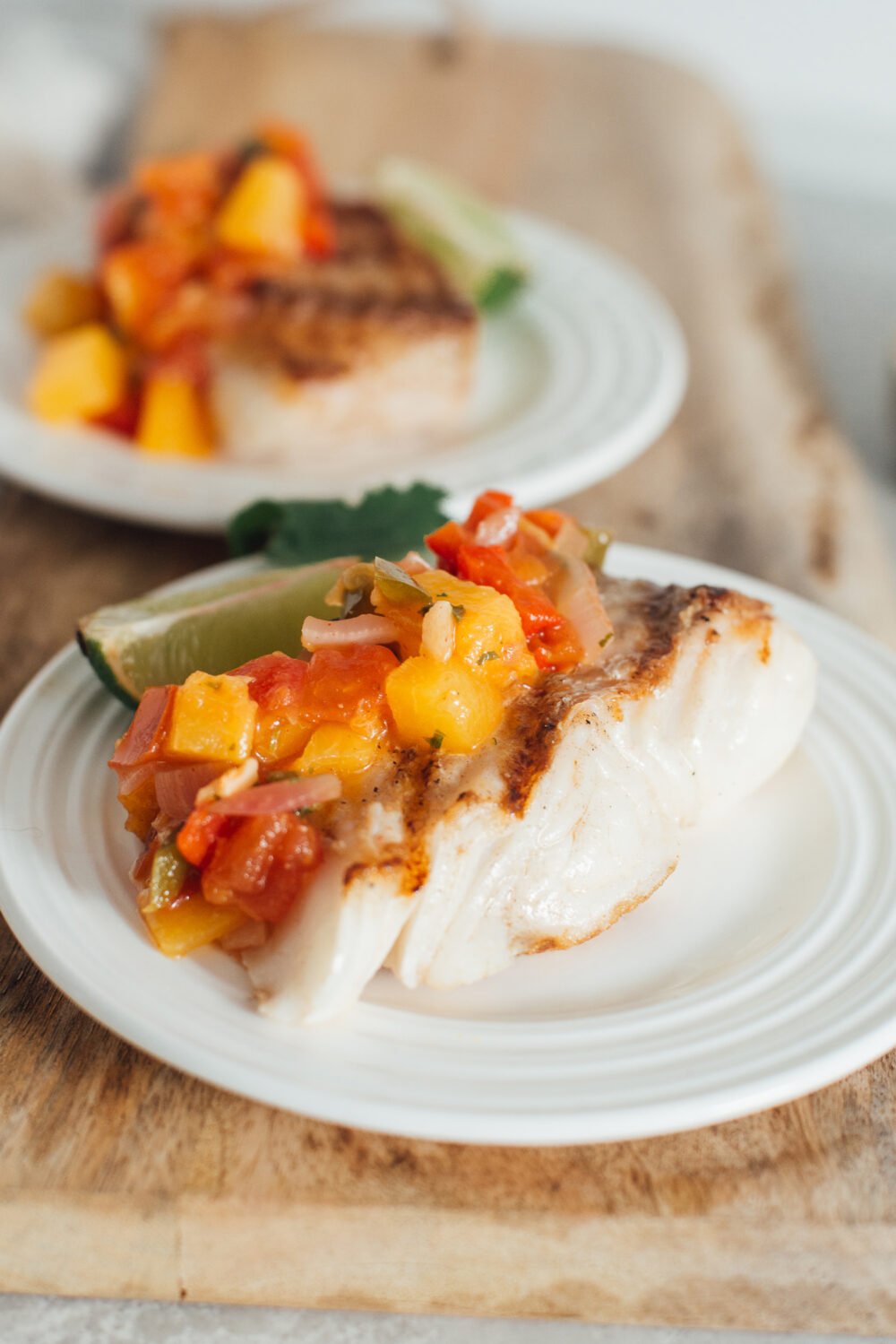 Portrait of two plates of grilled halibut with peach salsa on top.