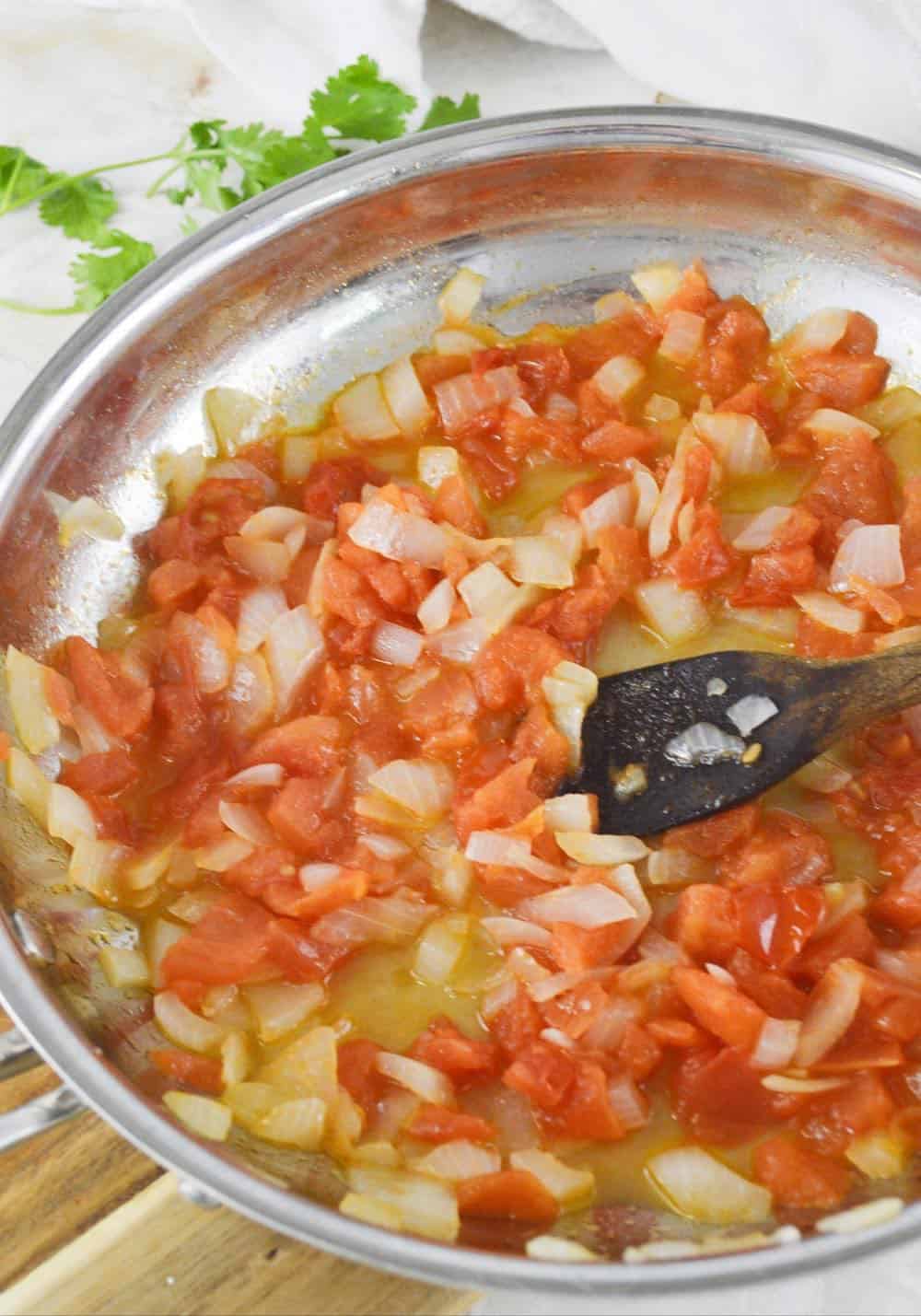 cooked onion and tomato in a skillet with a spoon.