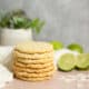Lime coconut cookies in a stack on a table with fresh limes.