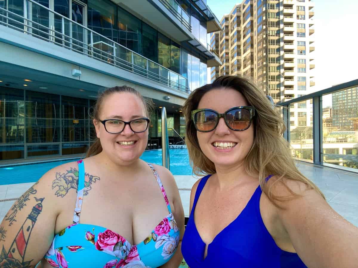 Two women in swim suits by the side of a hotel pool.