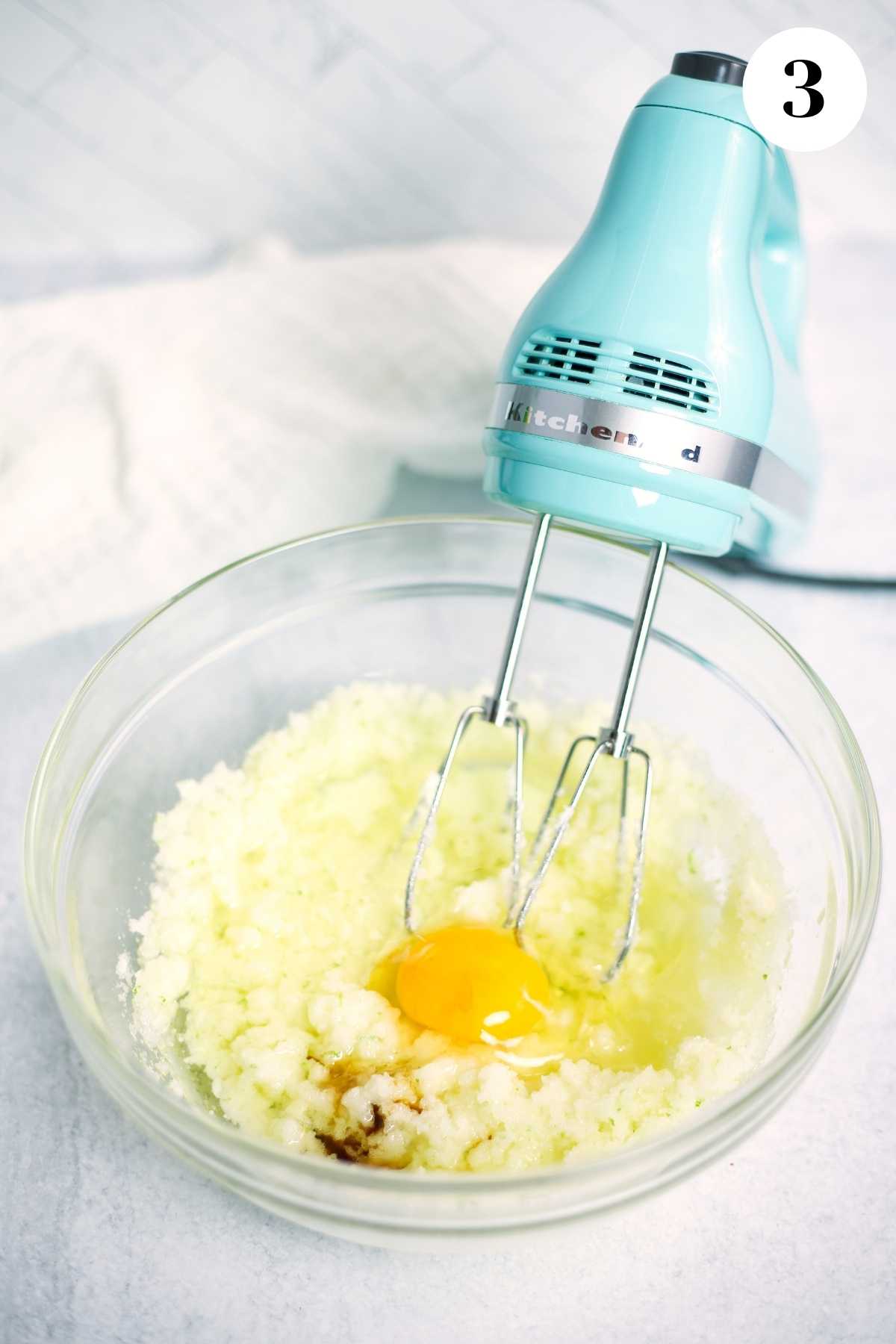 Sugar mixture with an egg added in a bowl with an electric mixer.