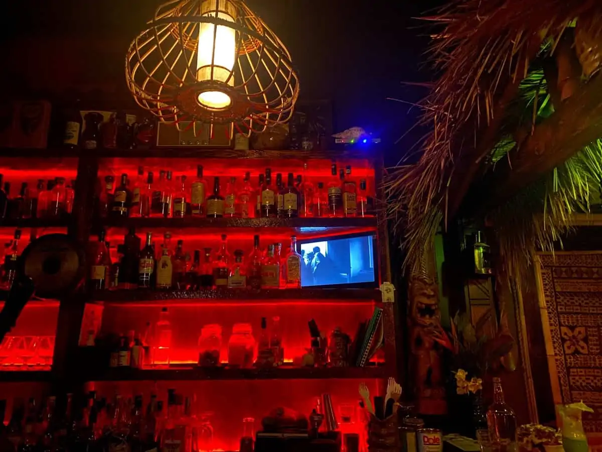 A wall in a bar with a red background highlighting bottles of alcohol on shelves.