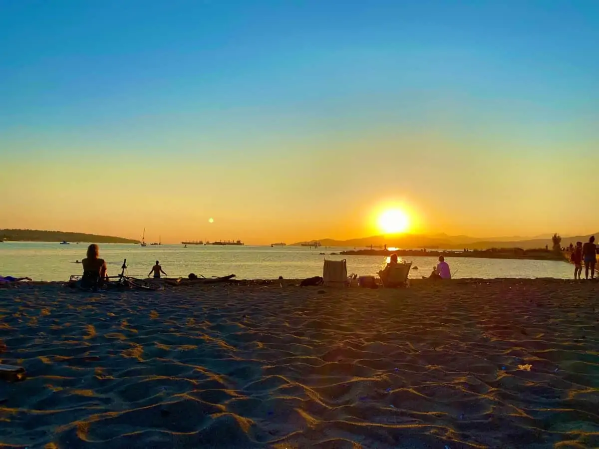 Sunset at the beach with the sand in the front and the sea and sky in orange and blue.