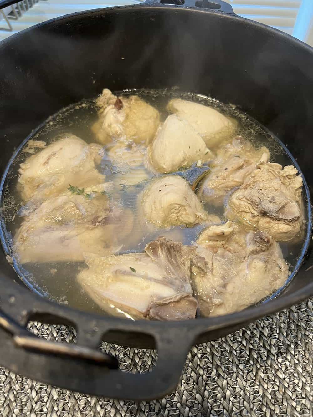Chicken cooking in water in a black Dutch Oven.