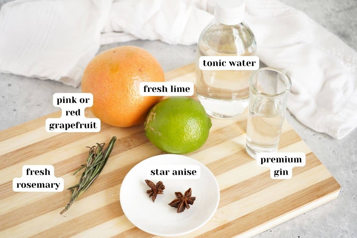 Fresh grapefruit, lime, star anise, fresh rosemary, gin and tonic water on a wooden cutting board.