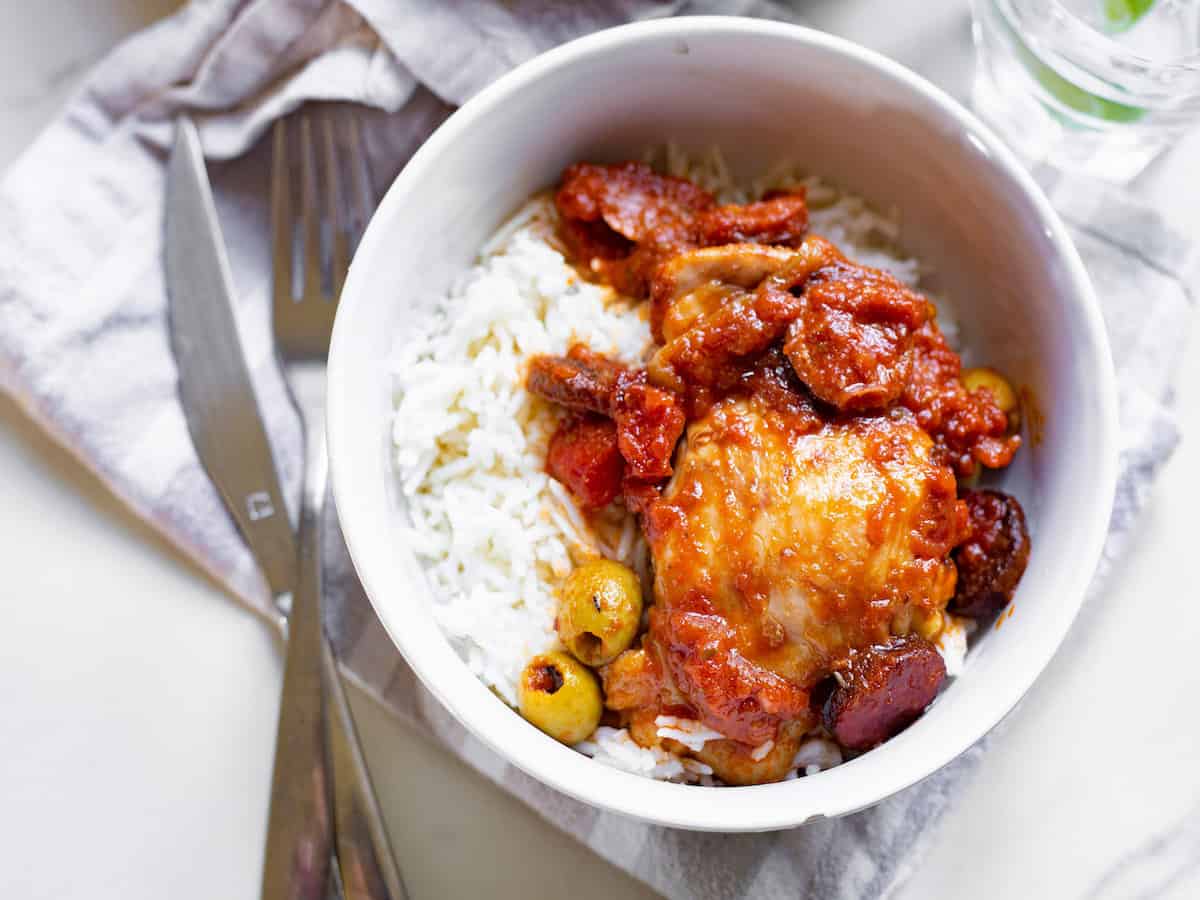 Spanish chicken and chorizo stew in a white bowl with rice. 