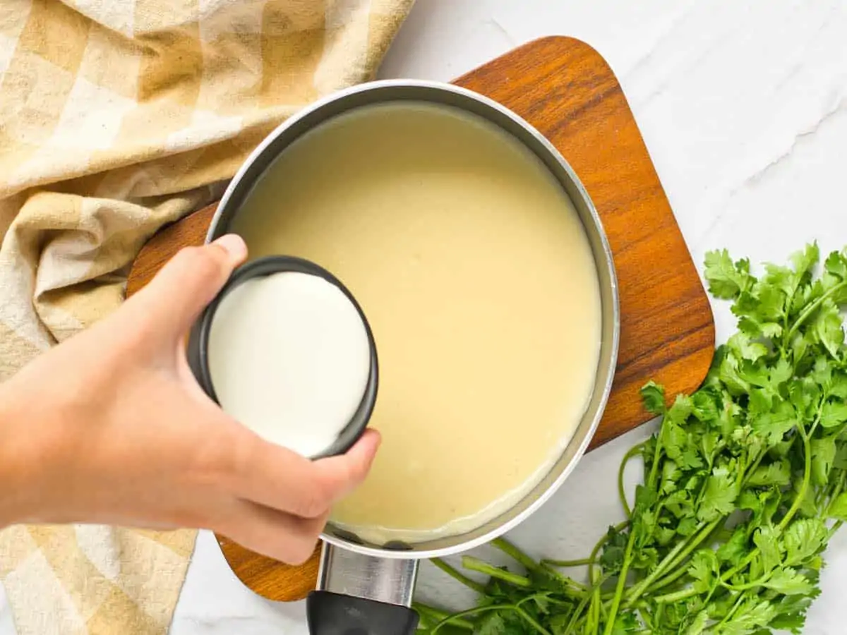 A woman's hand adding cream to Riesling soup in a pot.