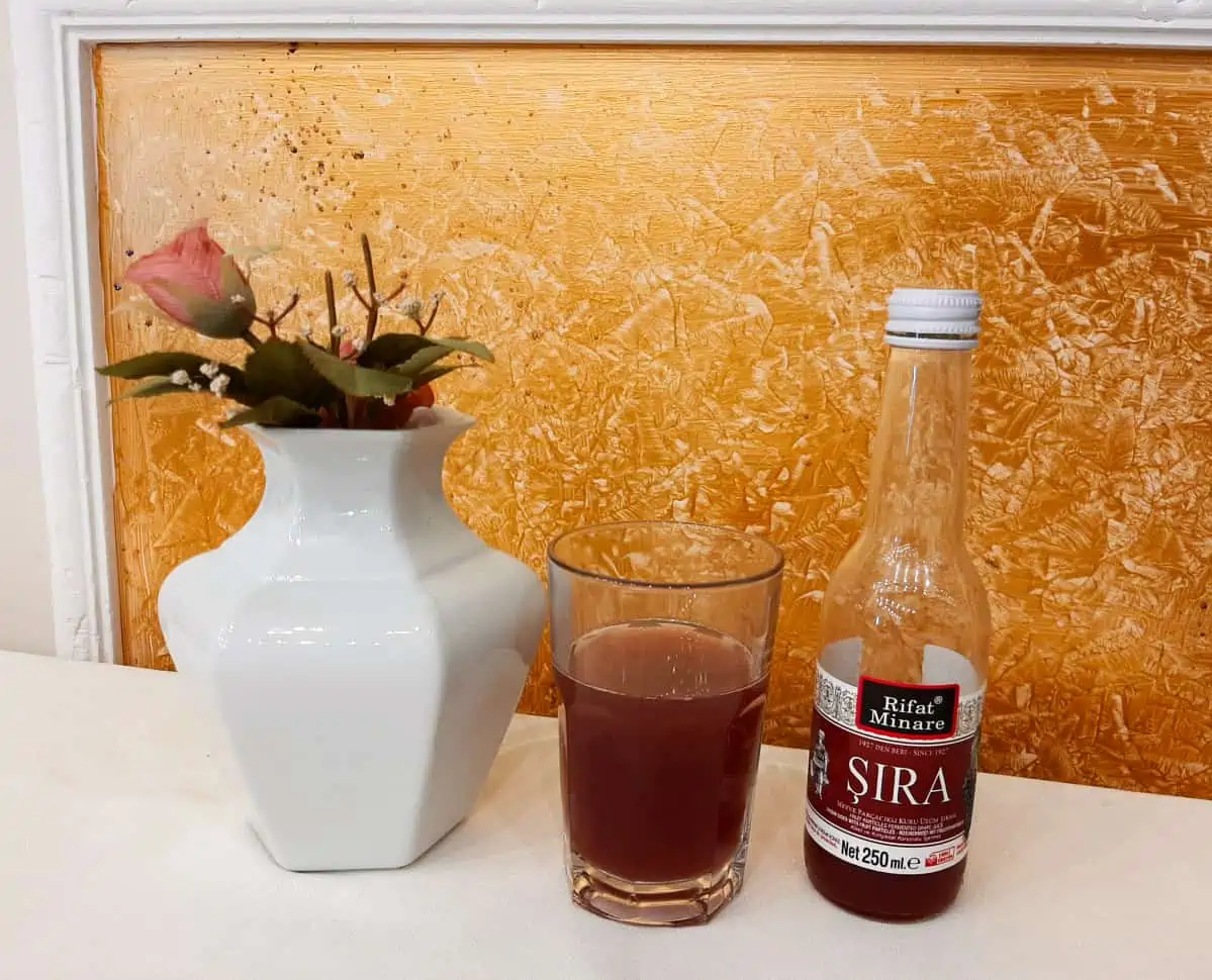 Sira in glass on table with white vase.