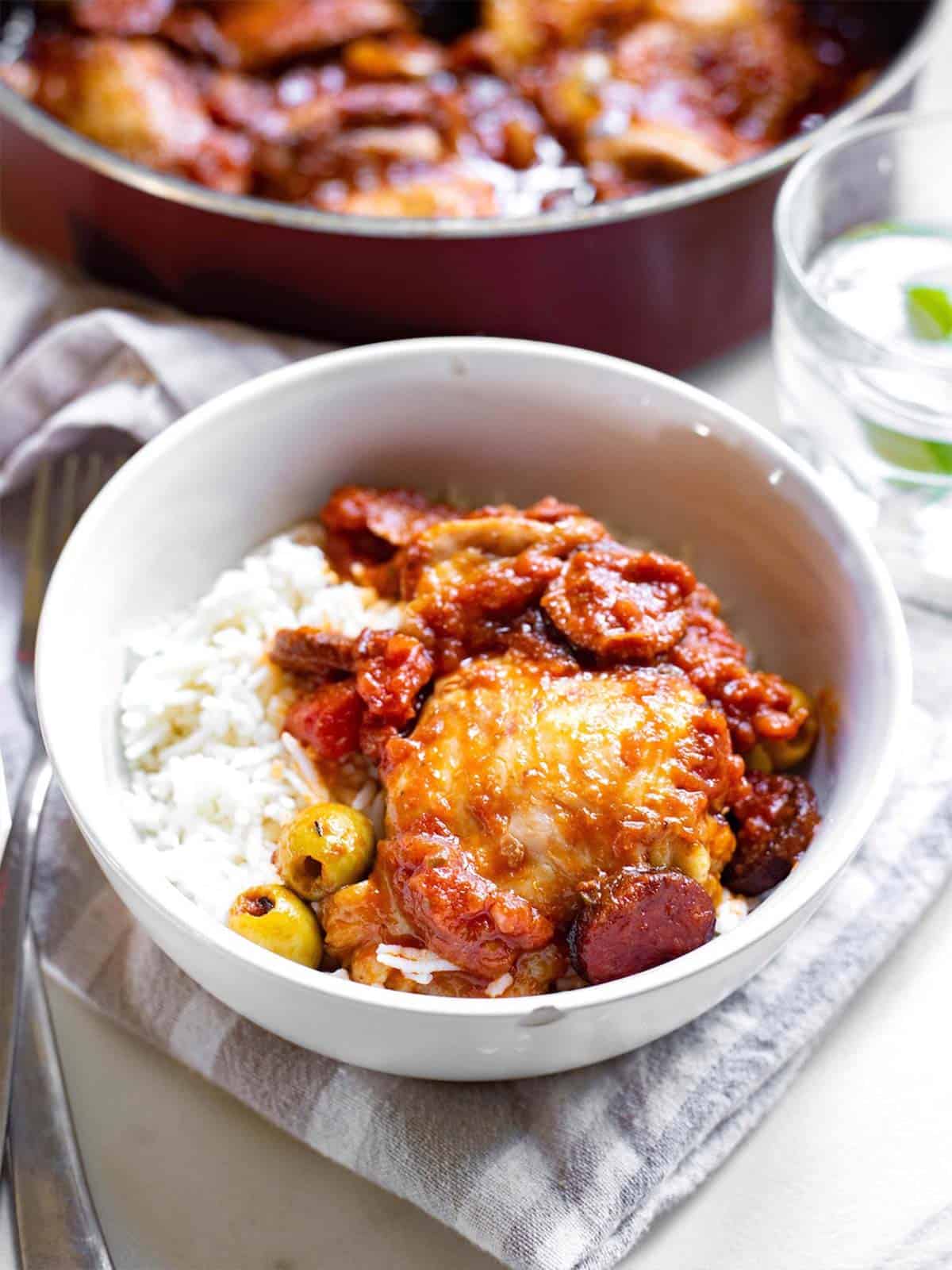 Spanish style chicken and chorizo stew in a white bowl with a fork and glass of water.