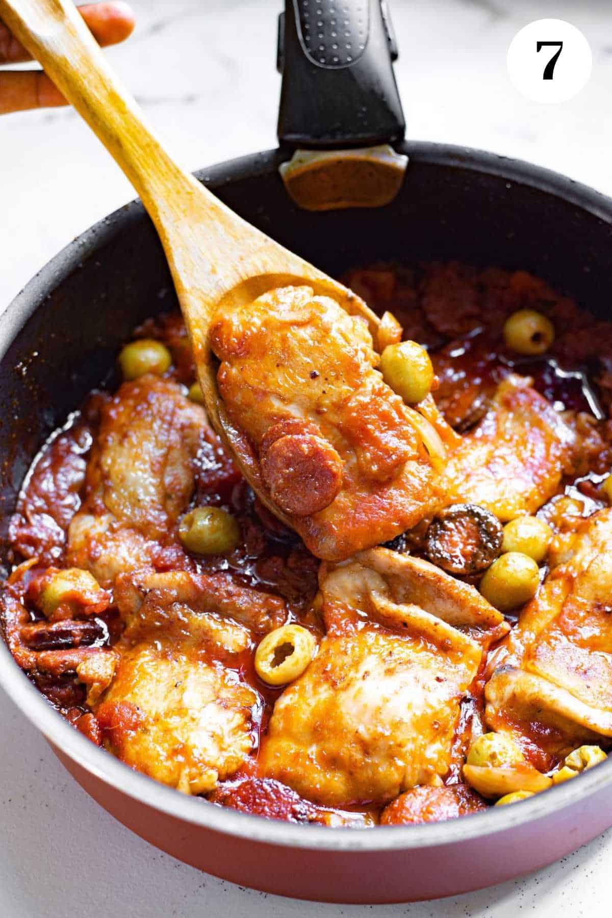 A person spooning Spanish stewed chicken with a wooden spoon.