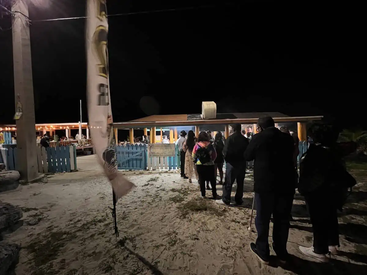 People lined up in front of beach shack for fish fry at night. 
