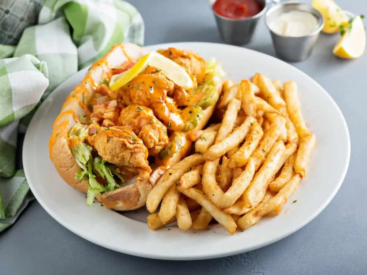 A shrimp Po Boy sandwich in New Orleans on a white plate with fries. 
