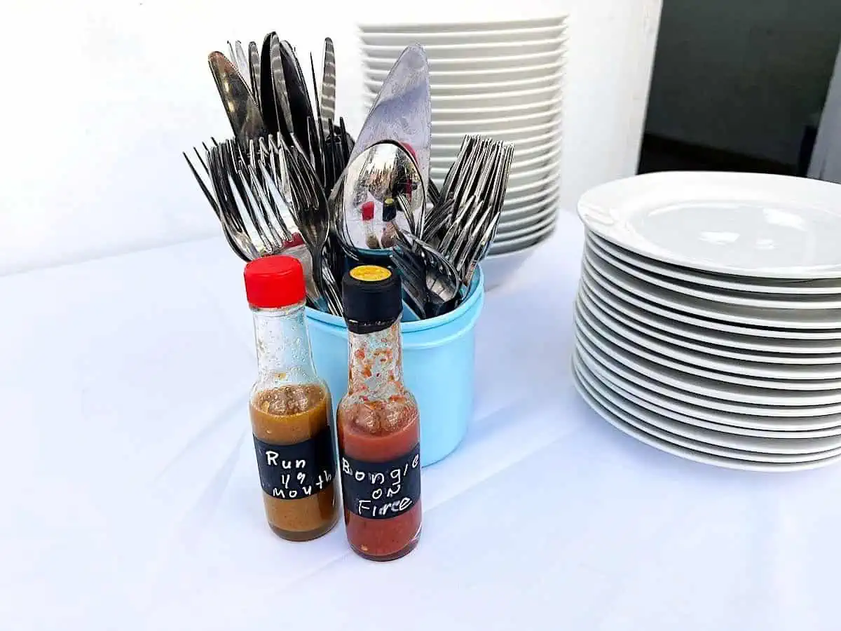 Two homemade sauce bottles on table with utensils and plates. 
