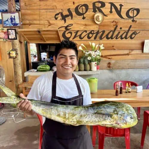 Young man holding a dorado fish in a Puerto Escondido restaurant.