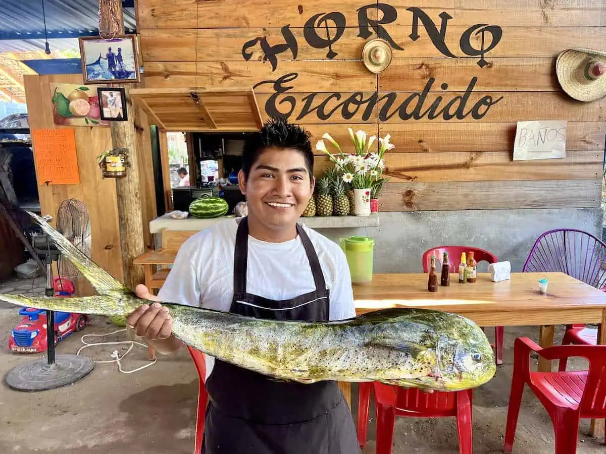 Young man holding a dorado fish that will be served baked in a clay oven. 