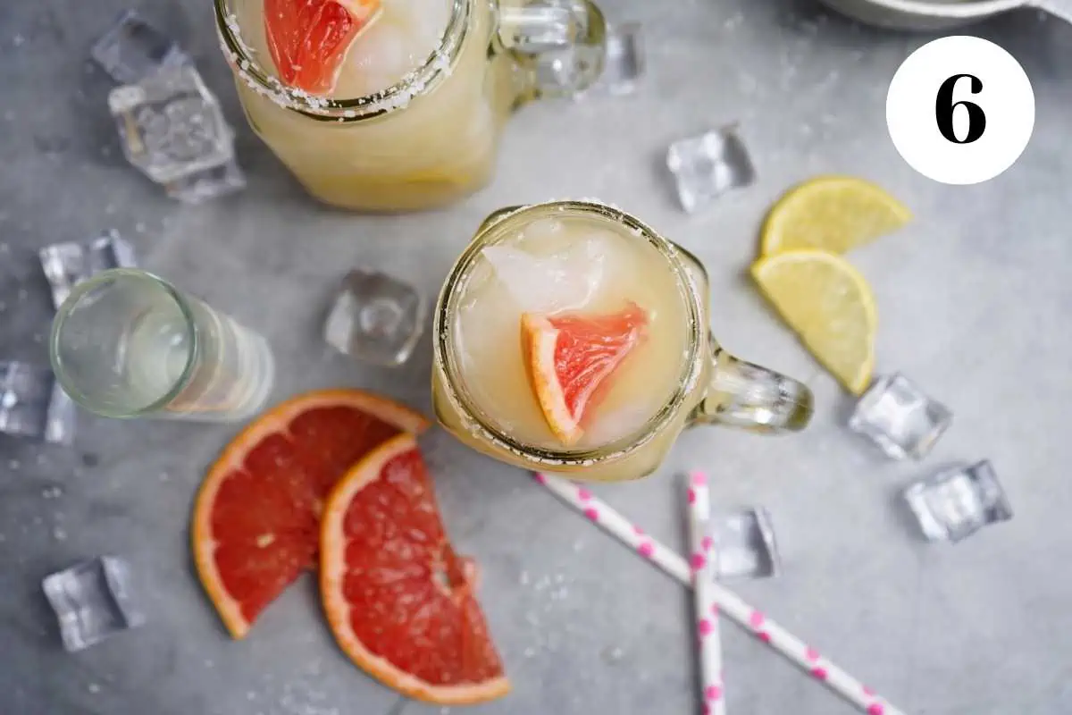 Finished grapefruit cocktails on the table with straws and grapefruit.