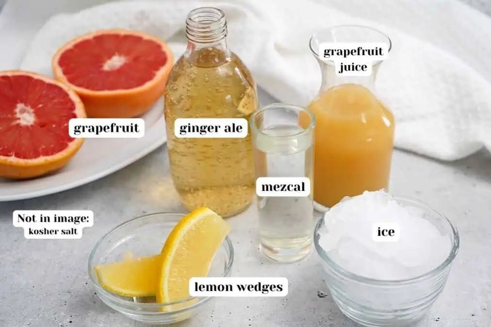 Ingredients to make mezcal grapefruit cocktail on the table with text labels.