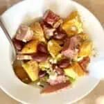 Mani salad in a white bowl with a spoon.