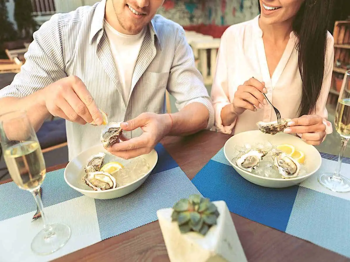 Two people eating oysters with a glass of wine. 