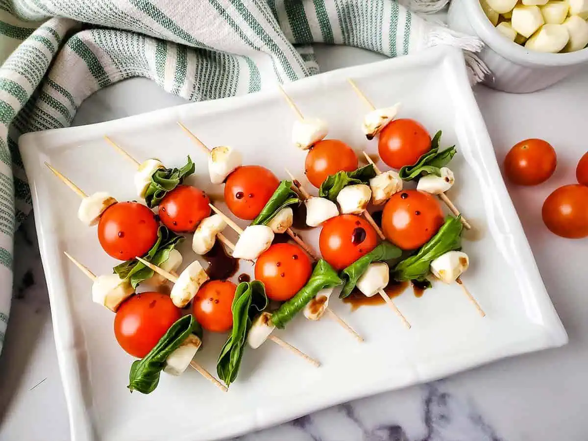 Caprese salad appetizer skewers on a platter with balsamic vinegar over the top.