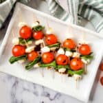 Caprese salad skewers on a platter with balsamic vinegar.