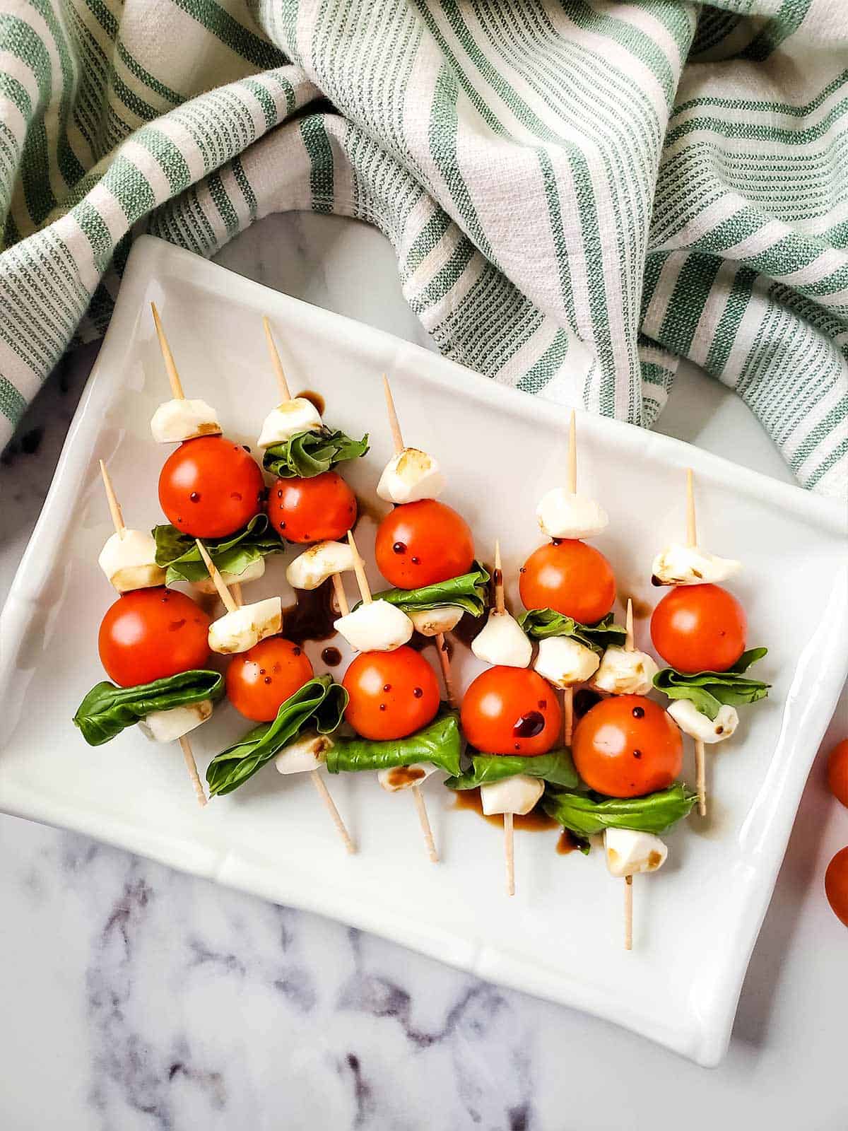 Caprese salad skewers on a white serving platter on the table with a linen napkin.