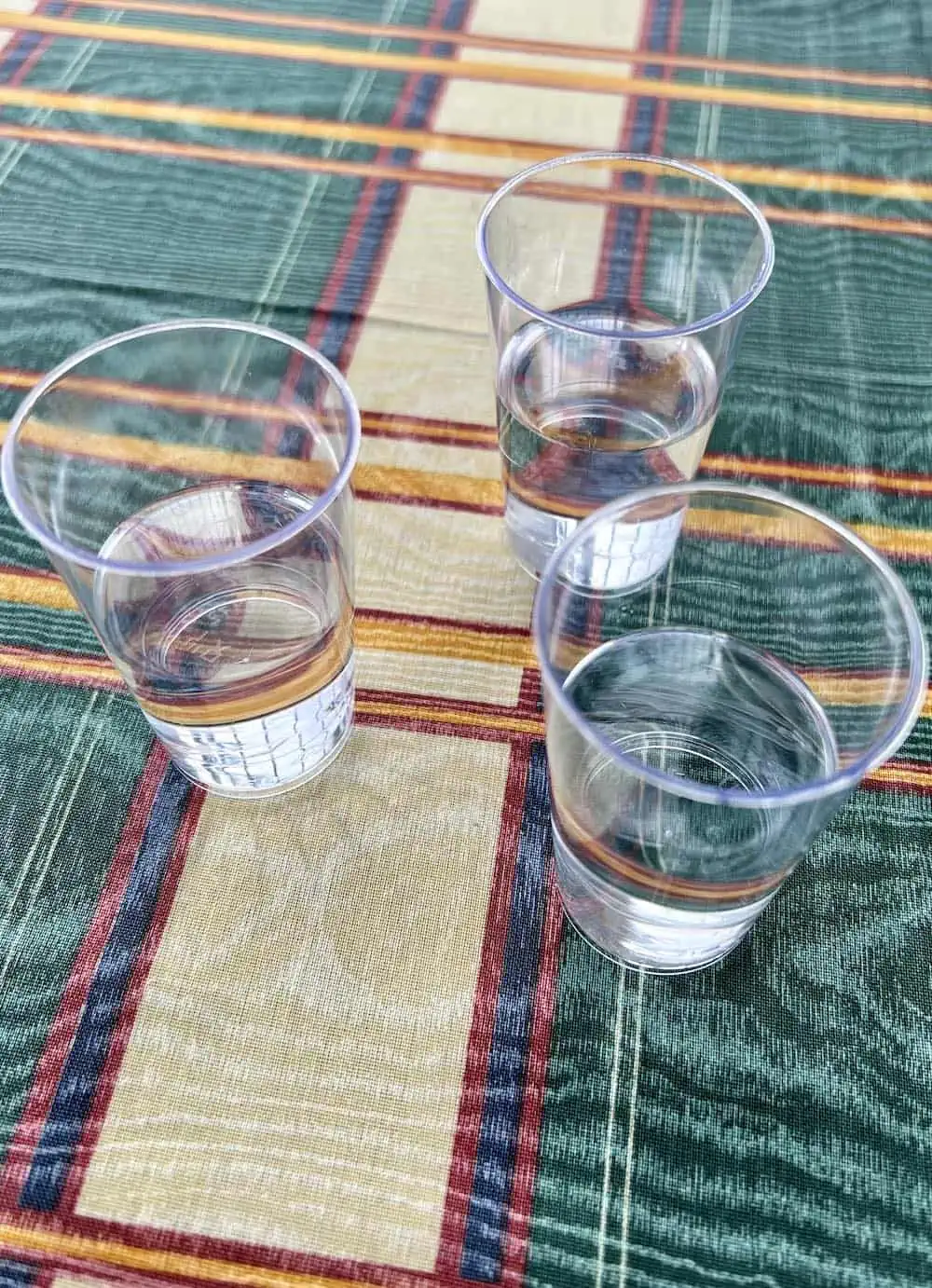 Three glasses of tsipouro on a plaid tablecloth in Greece. 