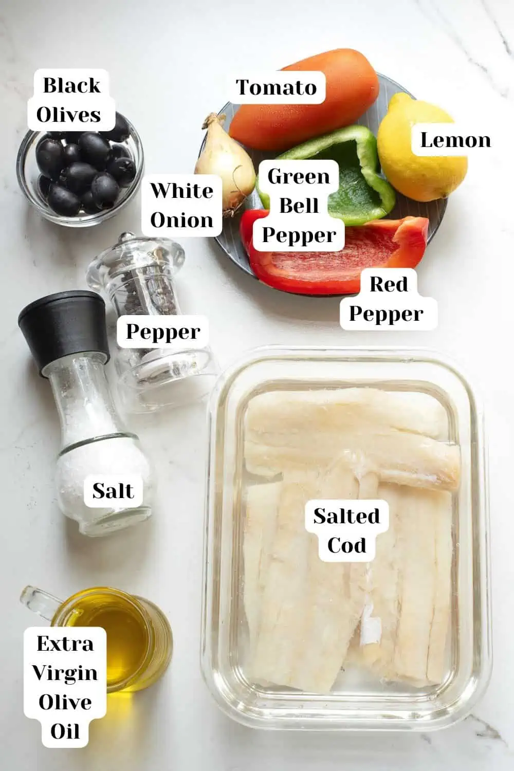 Ingredients for esueixada de bacalao including black olives, salted cod, white onion, tomato, lemon, red and green pepper, black pepper, salt and extra virgin olive oil, preferably Spanish. 