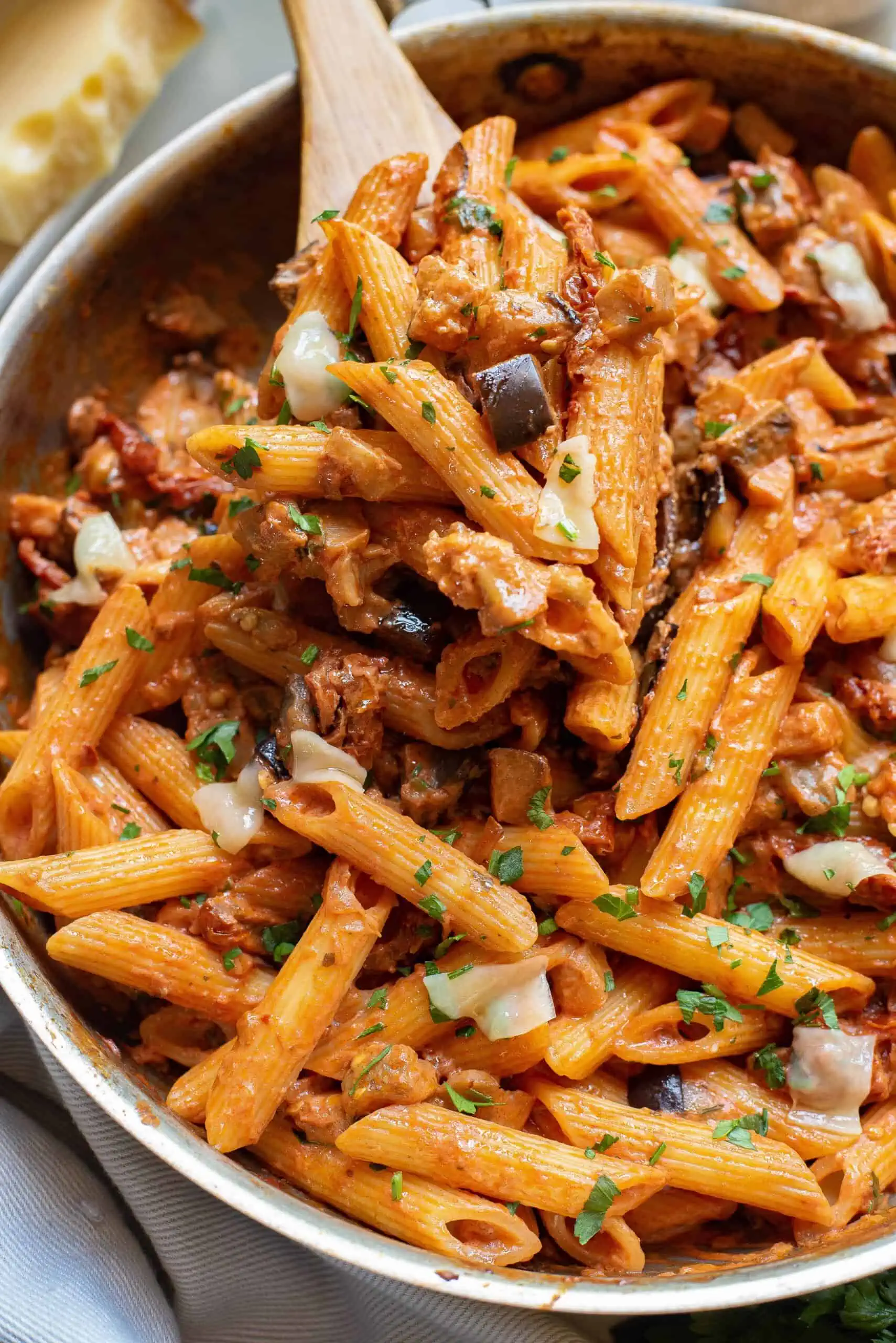 A close up of the  pasta with eggplant in the skillet and a wooden spoon.