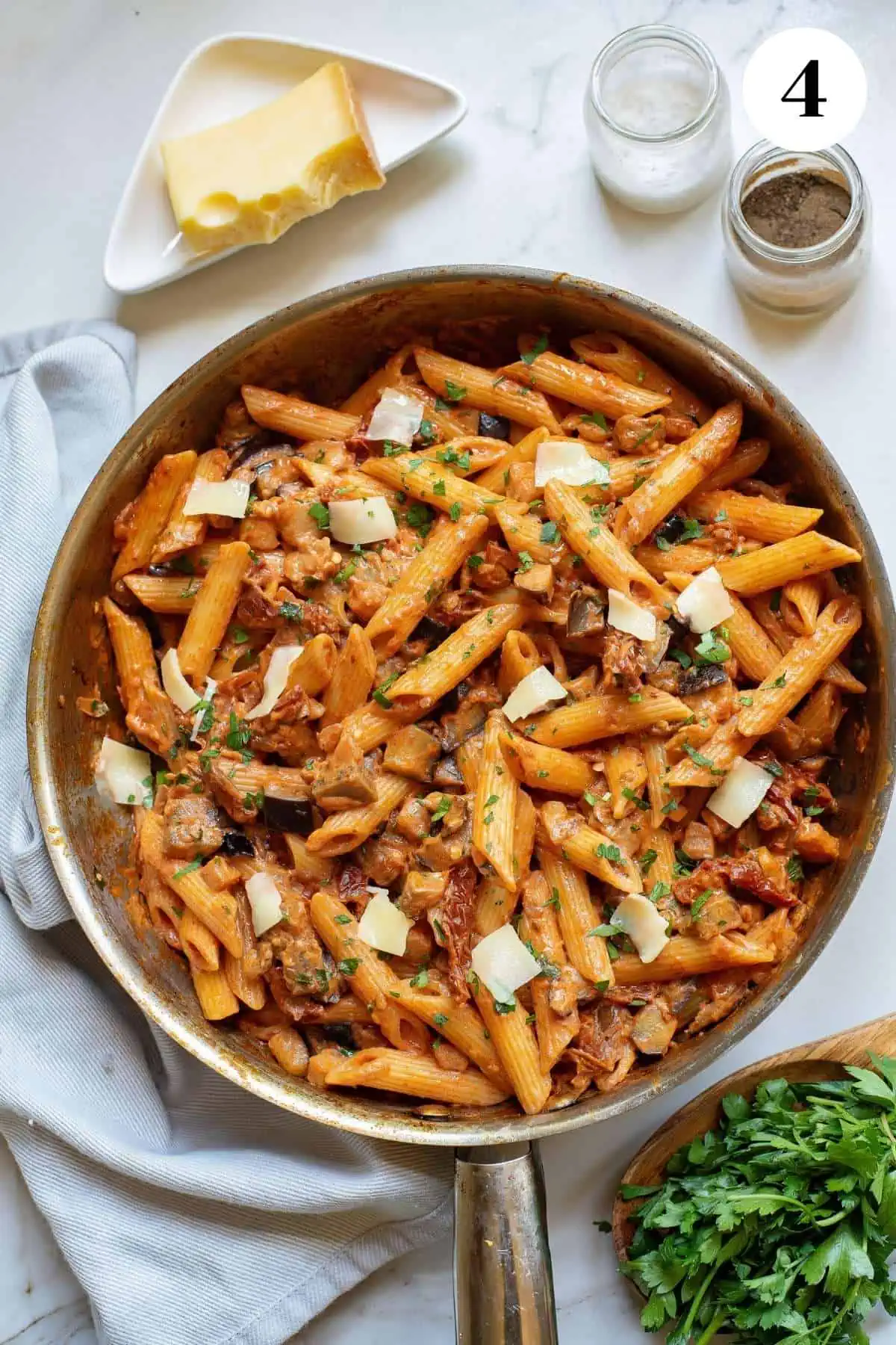 Finished creamy pasta with eggplant and sundried tomatoes in a skillet and topped with cheese and parsley.