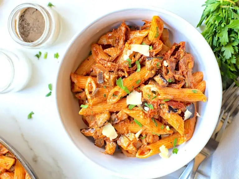 A bowl of pasta with sundried tomatoes and eggplant on the table with parsley garnish.