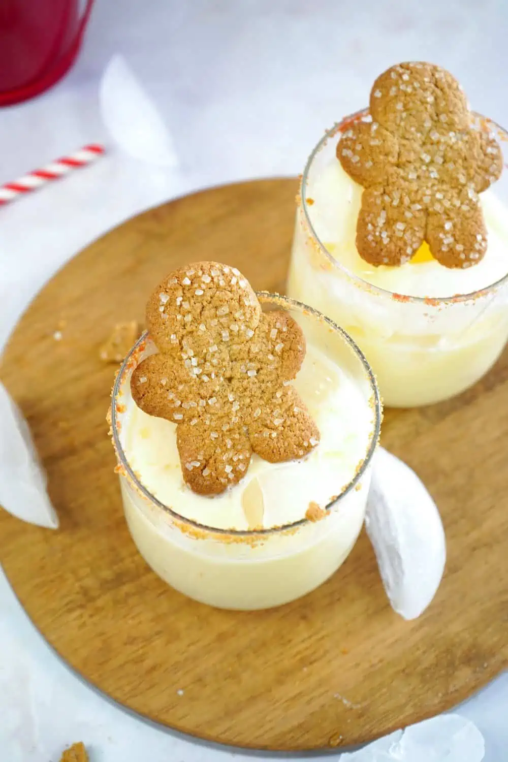 Eggnog cocktails decorated with a gingerbread man on a round wooden board.