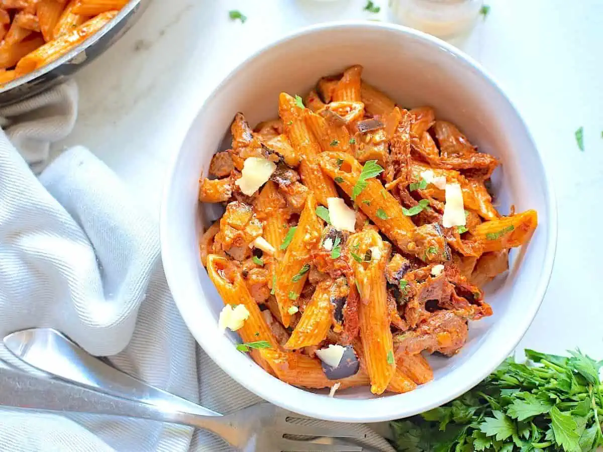 Creamy pasta with sun dried tomatoes in a white bowl with a fork. 