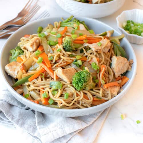 A bowl of guatemalan chow mein on the table with forks and a dish of green onions.