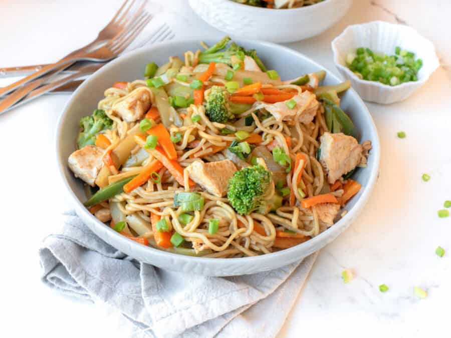 A bowl of guatemalan chow mein on the table with forks and a dish of green onions.