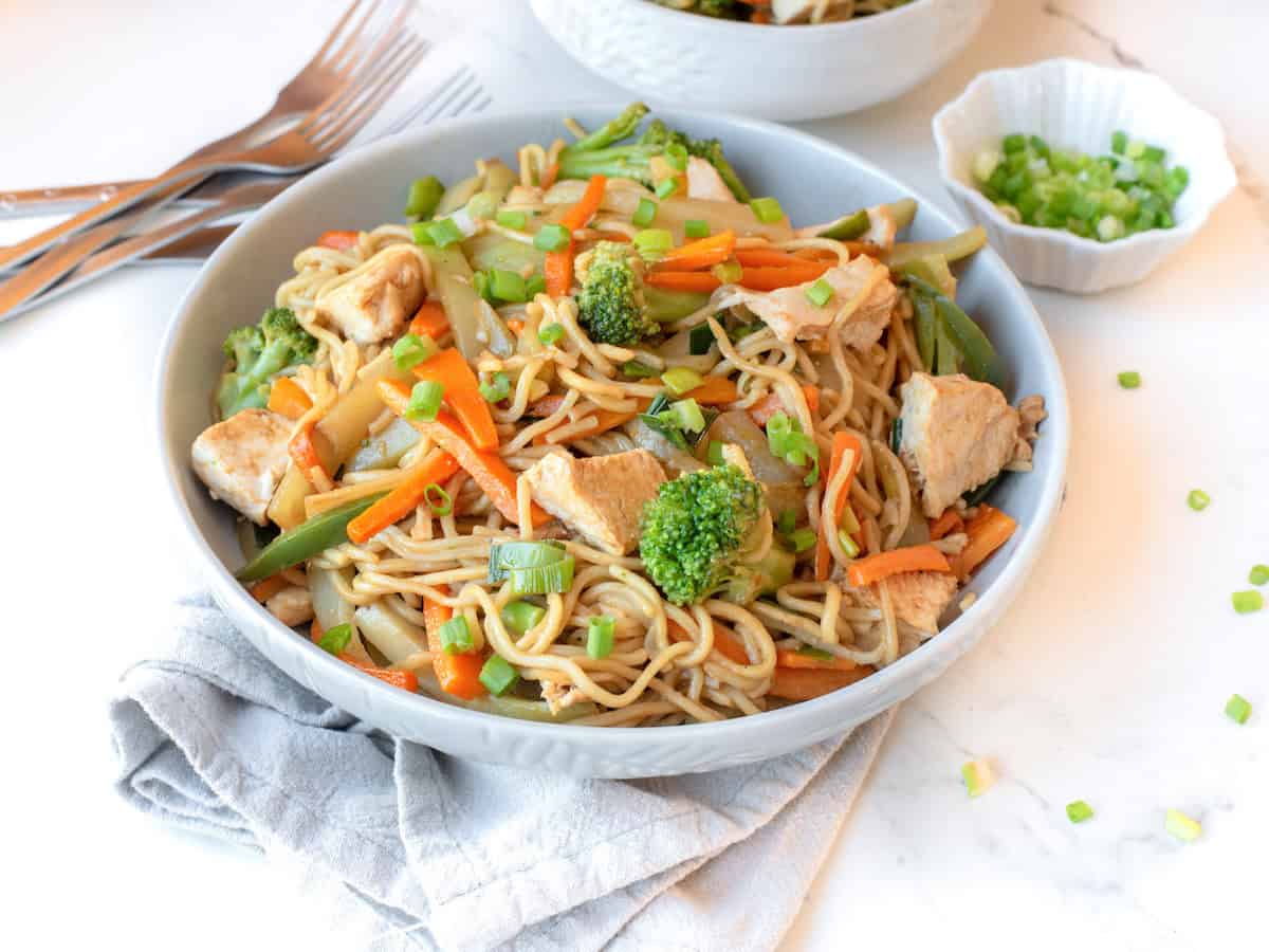 A bowl of guatemalan chow mein on the table with forks and a dish of green onions. 