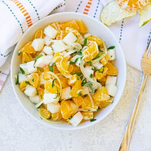 A bowl of jicama orange salad with a white tea towel in the back.