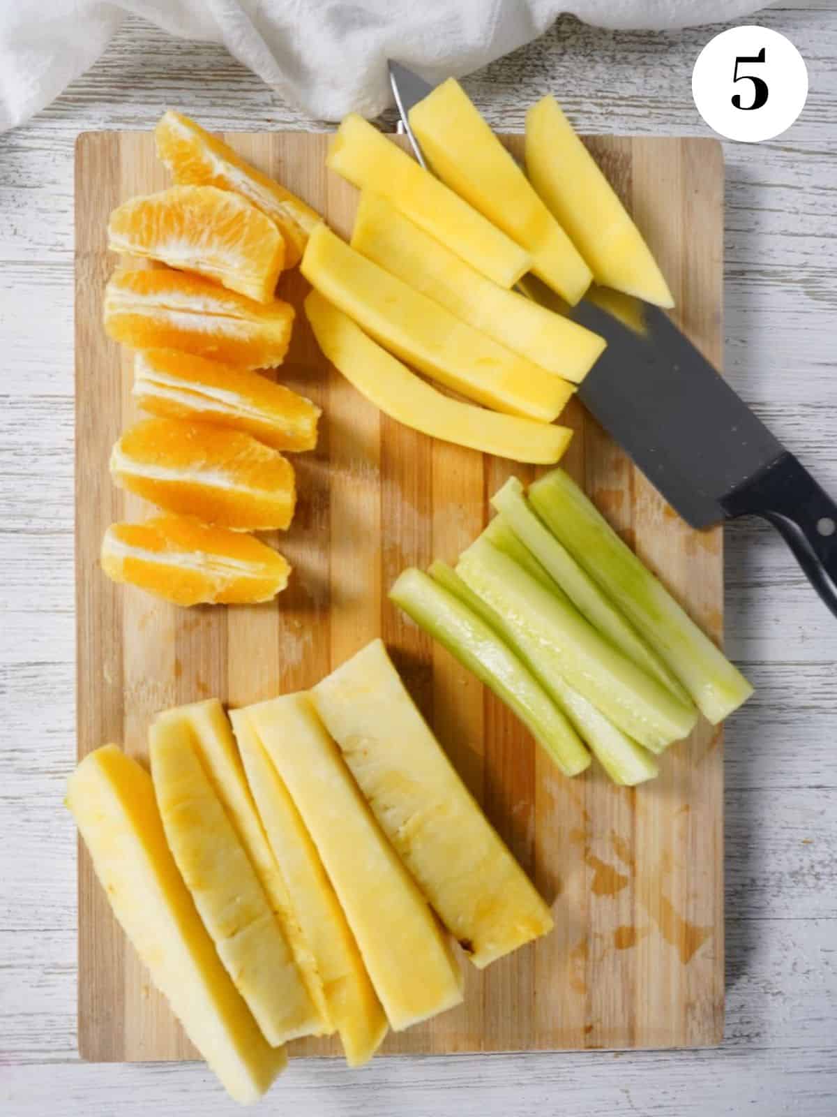 Pineapple, cucumber, orange, and mango prepped on a cutting board.