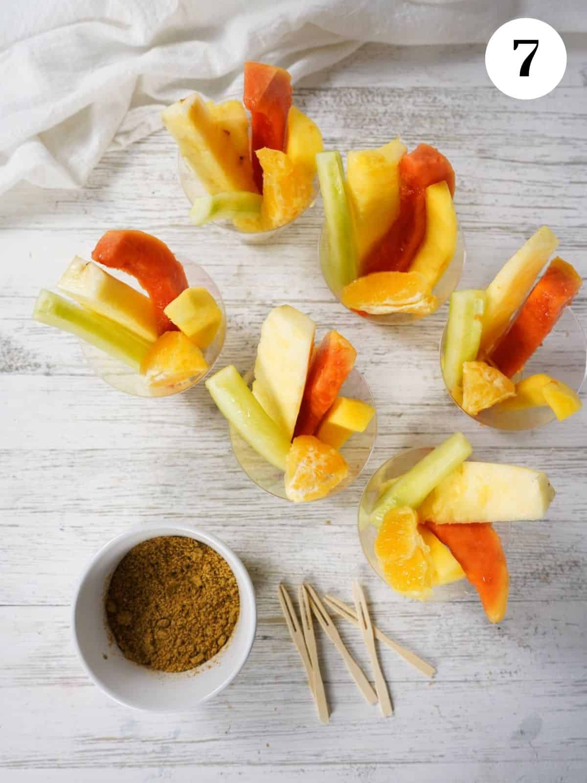 Fruit added to cups on a table next to wooden spears and a dish of the pepitoria.