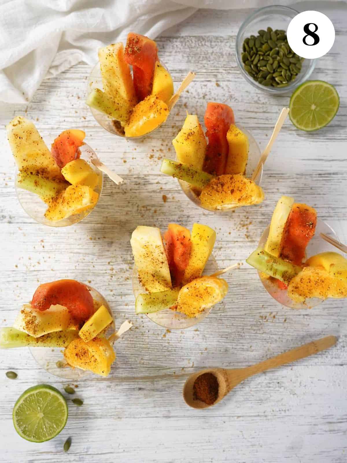 Ground pumpkin seeds mixture sprinkled on the fruit cups and some resting on a spoon to the side. 