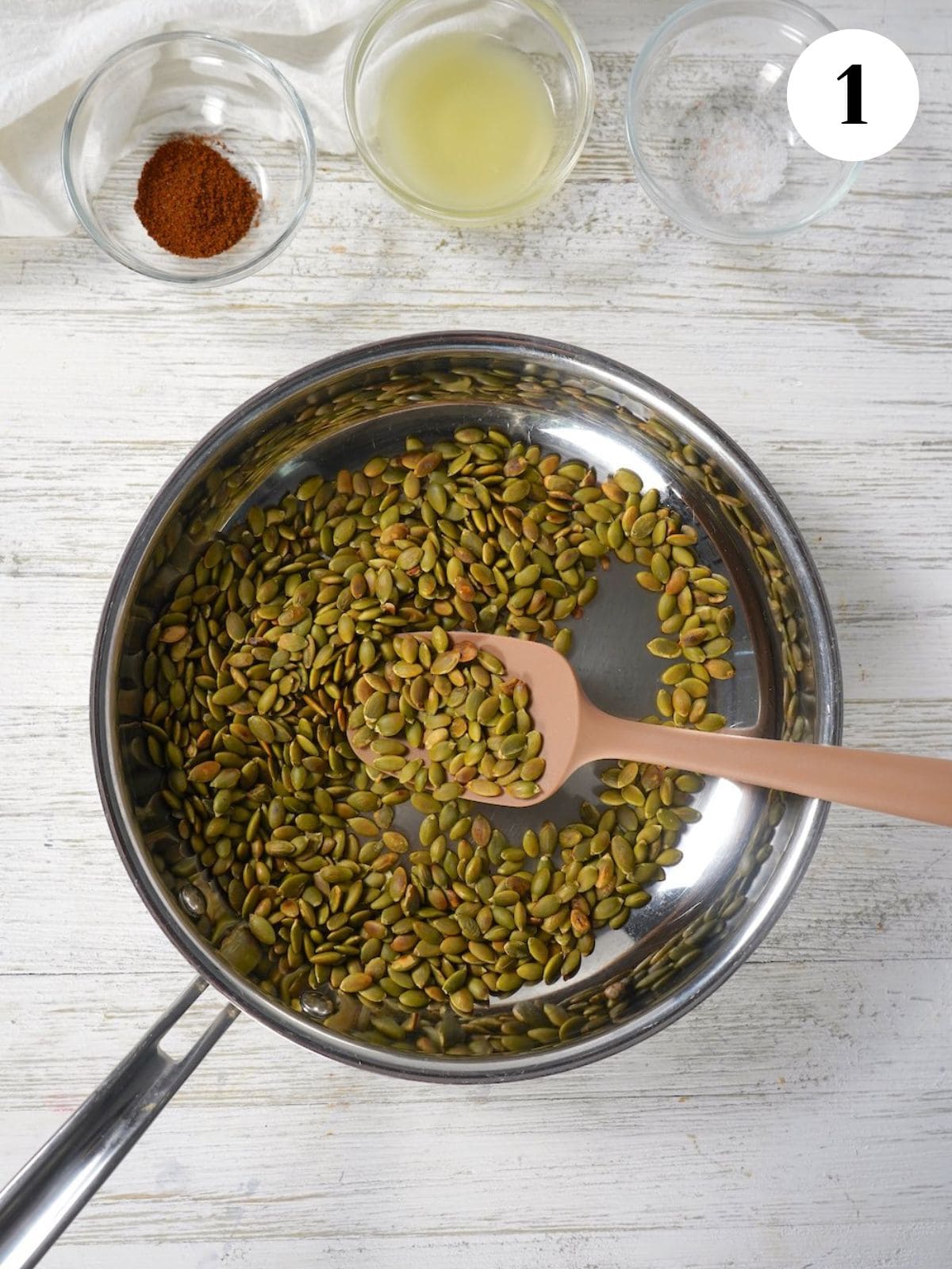 Pumpkin seeds in a skillet with a wooden spoon. 