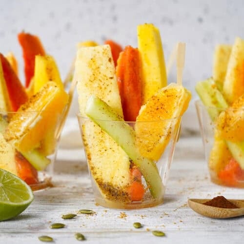 Three fruit cups sprinkled with pepitoria on a counter with a lime half to the side.